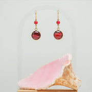 Red Flame Opal Earrings on a white background with a pink shell at the bottom of the image. 