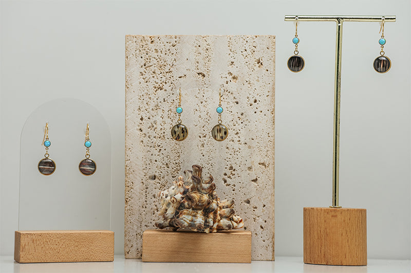 Three Blue Lagoon Opal Earrings stands on a white background with a slab of marble in the middle and shell at the base. 