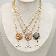 Three Whale Tail Necklaces on a cream necklace display bust. 