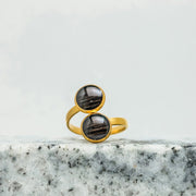 A Gold Double Pendant Adjustable Ring on black and white marble on a white background.