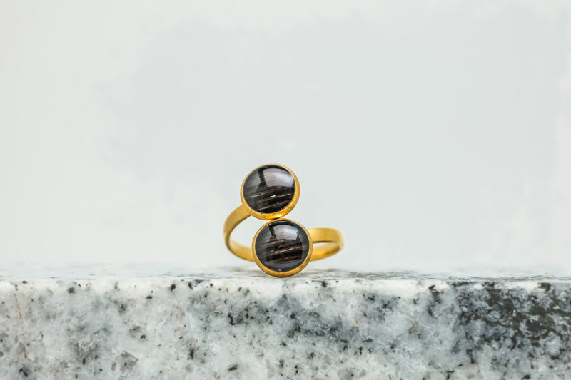 A Gold Double Pendant Adjustable Ring on black and white marble on a white background.
