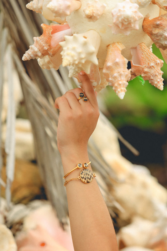 A hand and arm showing two bracelets and a ring reaching up to shells. 