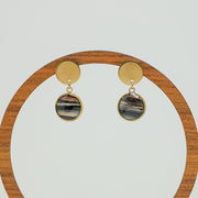 Round Golden Earrings on a circular wooden stand on a white background. 