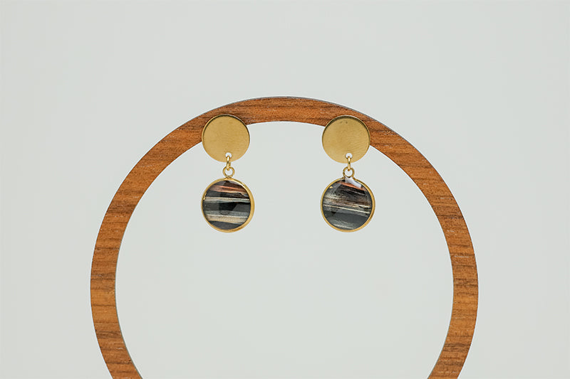Round Golden Earrings on a circular wooden stand on a white background. 