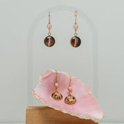 two Seashell Pink Opal Earrings on a white background with a pink shell at the bottom of the image. One pair is in the shell. 