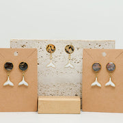 Three pairs of Freshwater Pearl Whale Tail Earrings on stands on white marble on a white background.