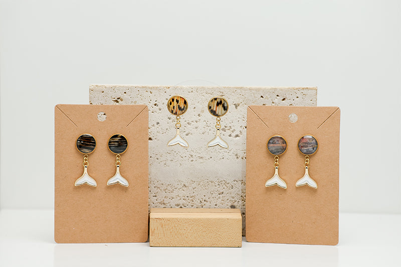Three pairs of Freshwater Pearl Whale Tail Earrings on stands on white marble on a white background.