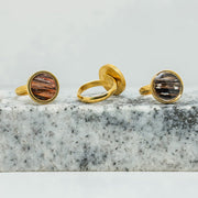 Three Gold Adjustable Rings on black and white marble on a white background.