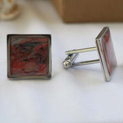 Close-up image of a set of square Cuff Links on a white tablecloth with a shell and a jewelry box in the background.