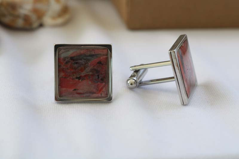 Close-up image of a set of square Cuff Links on a white tablecloth with a shell and a jewelry box in the background.