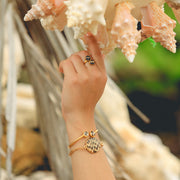 A hand and arm showing two bracelets and a ring reaching up to shells. 