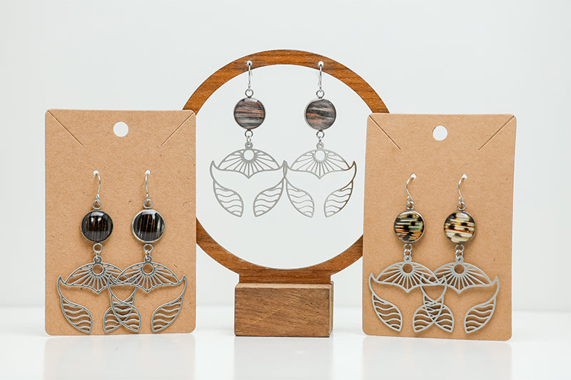 Three pairs of Silver Whale Tail Earrings on stands on a white background. 