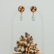 A pair of Larimar Teardrop Posts on a white background with a shell at the bottom of the image.