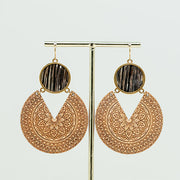 Wooden Mandala Statement Earrings dangle from a gold rod stand on a white background. 