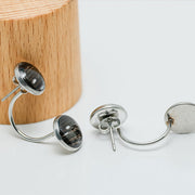Ear Jacket Post Earrings near a circular wooden stand on a white background.  
