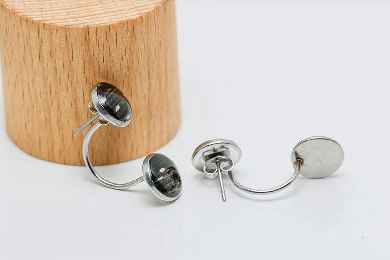 Ear Jacket Post Earrings near a circular wooden stand on a white background.  