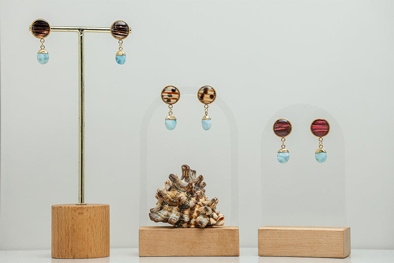 Three pairs of Larimar Teardrop Posts on stands on a white background with a shell at the bottom of the image.