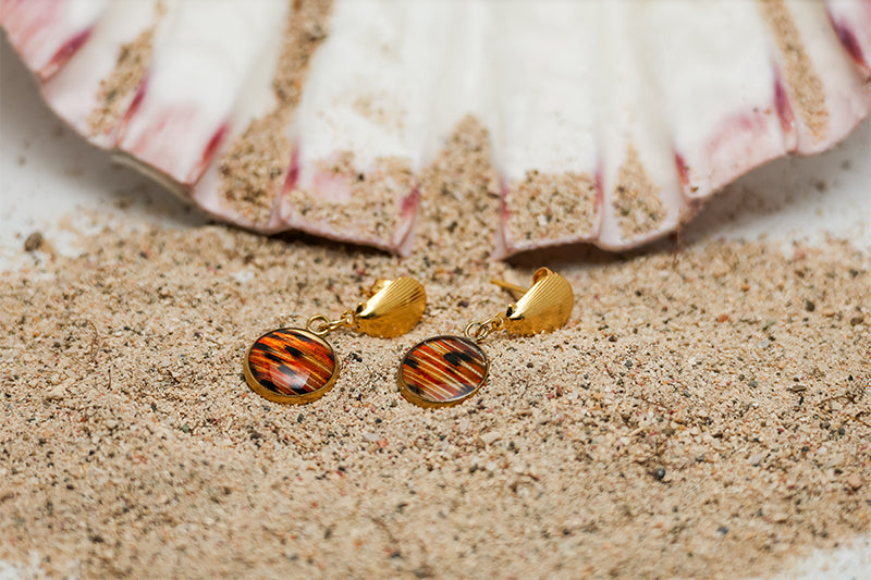 Petite Shell Earrings on sand with a pink clam shell in the background. 