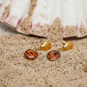 Petite Shell Earrings on sand with a pink clam shell in the background. 