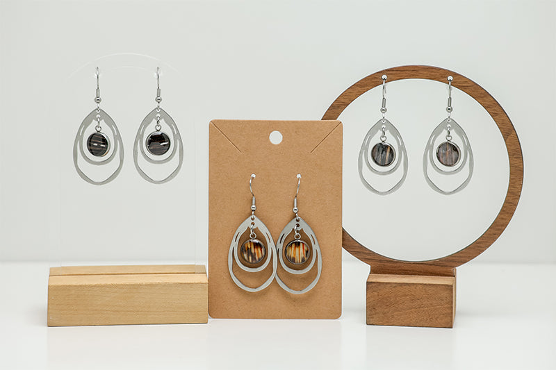 Three pairs of Silver Teardrop Earrings on stands on a white background.