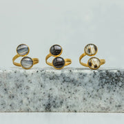 Three Gold Double Pendant Adjustable Rings on black and white marble on a white background.