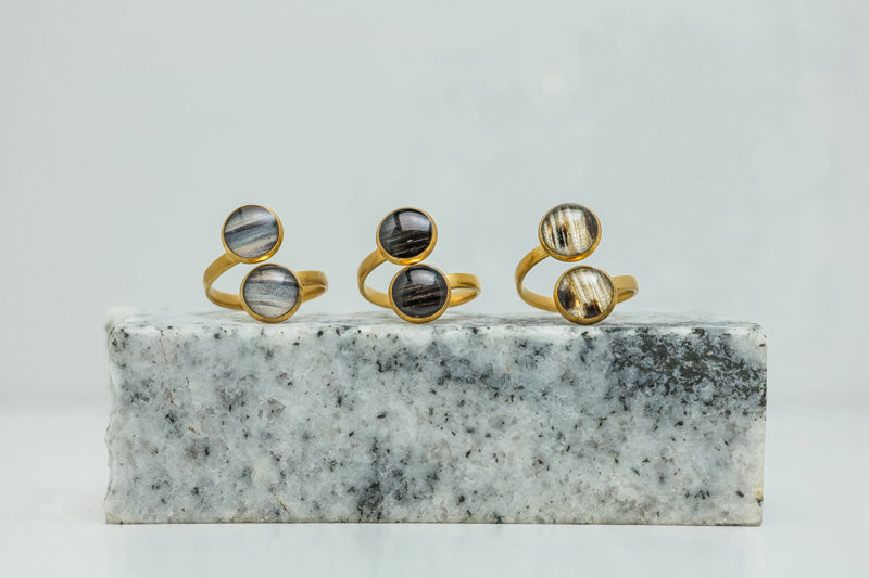 Three Gold Double Pendant Adjustable Rings on black and white marble on a white background.
