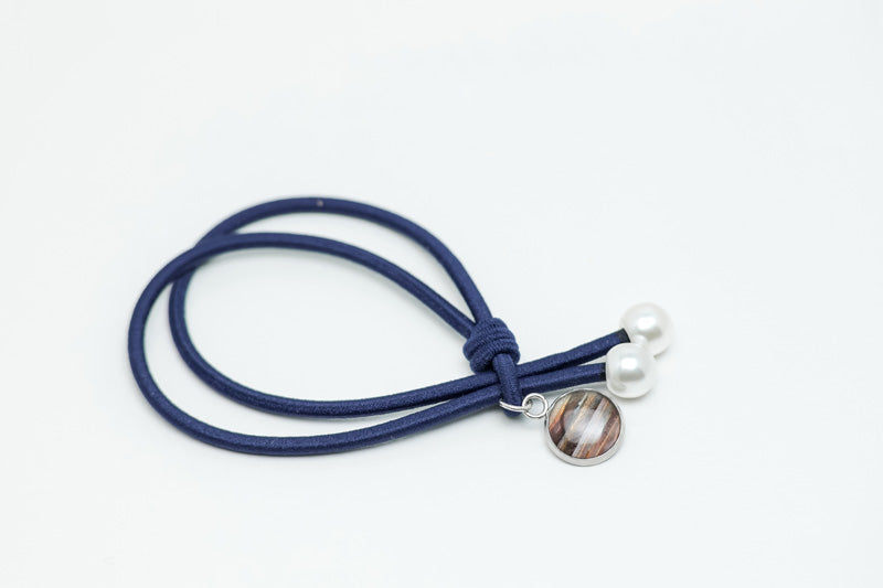 Blue hair tie with two pearls and a lionfish charm at the end on a white background.