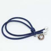 Blue hair tie with two pearls and a lionfish charm at the end on a white background.
