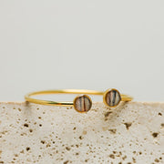 A Gold Double Pendant Cuff on white marble on a white background.