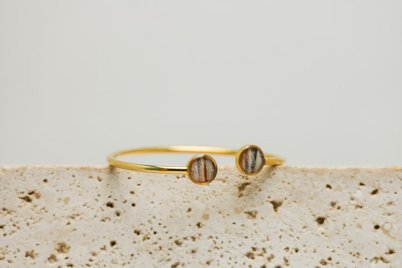 A Gold Double Pendant Cuff on white marble on a white background.