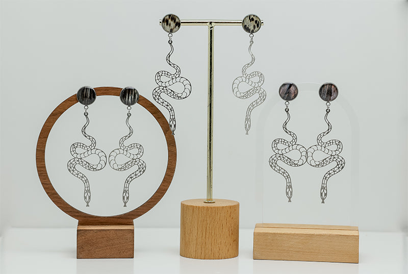 Three pairs of Snake Earrings on stands on a white background. 