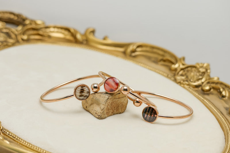 Three Rose Gold Cuffs on a rock on a white background with gold frame.