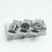Three Money Clips on a piece of black and white marble on a white background. 