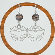 Silver Whale Tail Earrings on a circular wooden stand on a white background. 