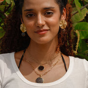 A woman in a white t-shirt wearing two necklaces and a pair Bold Golden Disc Earrings in front of a tree.