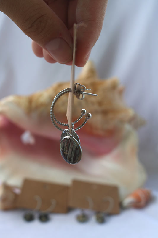 Close-up of Fingers holding a cardboard stand with Silver Open Hoop Posts. A shell and two other pairs are in the background.