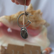 Close-up of Fingers holding a cardboard stand with Silver Open Hoop Posts. A shell and two other pairs are in the background.