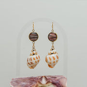 A pair of Leopard Conch Shell Dangles on a white background with a pink shell at the bottom of the image. 