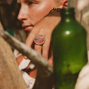  A woman's hand and face behind a glass green bottle and driftwood wearing a Gold Statement Ring.