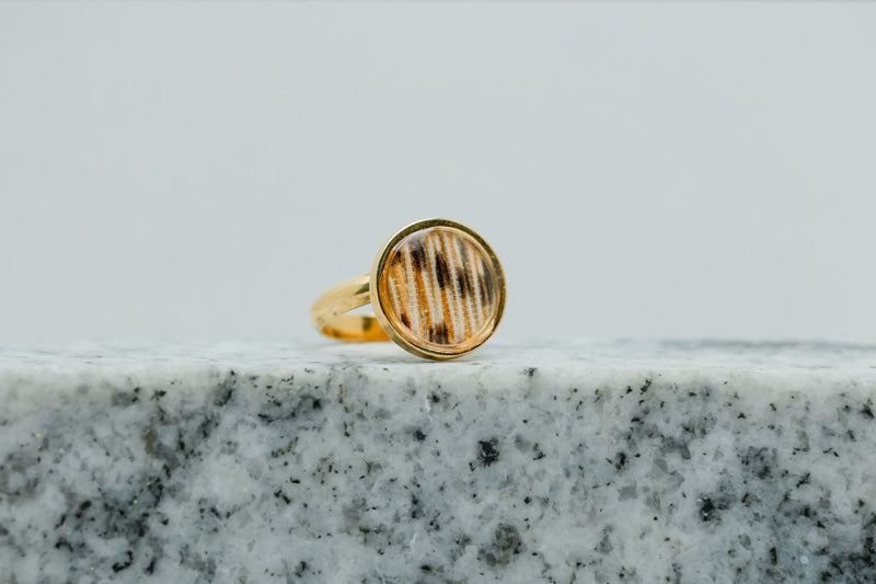 A Gold Adjustable Ring on black and white marble on a white background.
