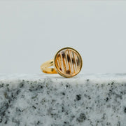 A Gold Adjustable Ring on black and white marble on a white background.