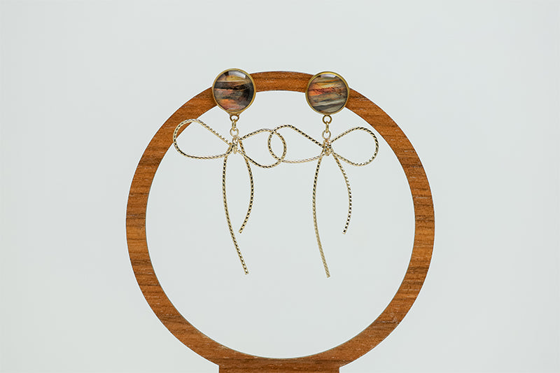 Bows Before Bros Earrings on a circular wooden stand on a white background.  