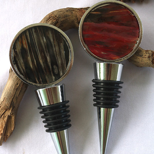 Two Wine Bottle Stoppers on a piece of driftwood on a white background. 