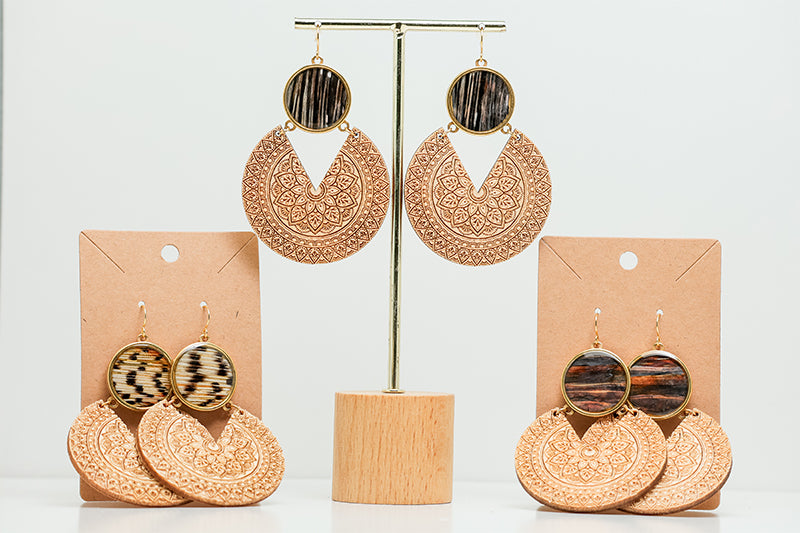 Three Wooden Mandala Statement Earring pairs on stands on a white background. 
