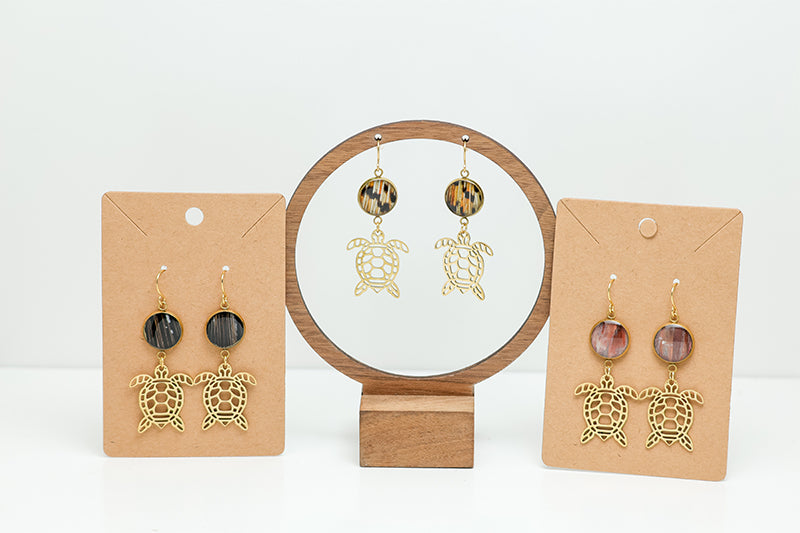 Three pairs of Golden Turtle Earrings on stands on a white background. 