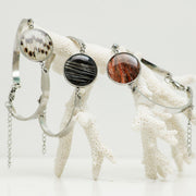 Three Round Silver Bracelets hanging from white coral on a white background. 