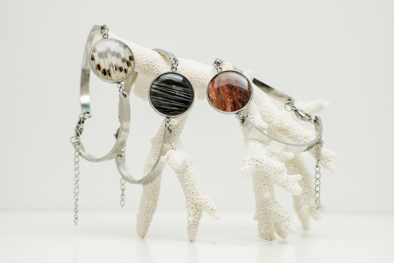 Three Round Silver Bracelets hanging from white coral on a white background. 