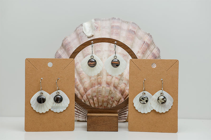 Three pairs of Iridescent Mother of Pearl Dangles on stands on a white background with a clam shell also in the background.  