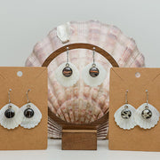Three pairs of Iridescent Mother of Pearl Dangles on stands on a white background with a clam shell also in the background.  