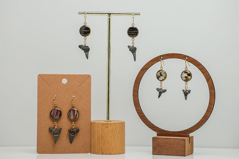 Three Shark Tooth Gold Dangles Earrings on stands on a white background. 